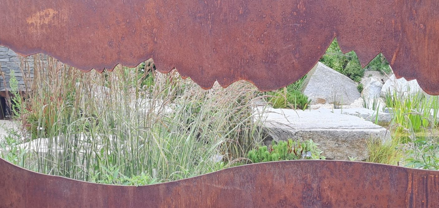 Mauer Beet Bunte Blumen und Gräser in einer Gartenlandschaft mit runden Hecken.